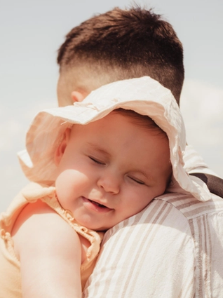 Baby in sun hat leaning on dad's shoulder