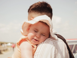 Baby in sun hat leaning on dad's shoulder