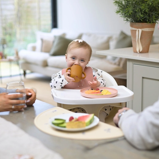 Baby sat in highchair at table eating with mum and dad