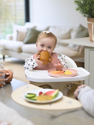 Baby sat in highchair at table eating with mum and dad