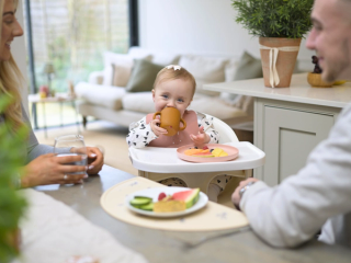 Baby sat in highchair at table eating with mum and dad