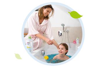 Frau in hellem Nachthemd kniet neben Badewanne, in der Kind mit Spielzeugente sitzt