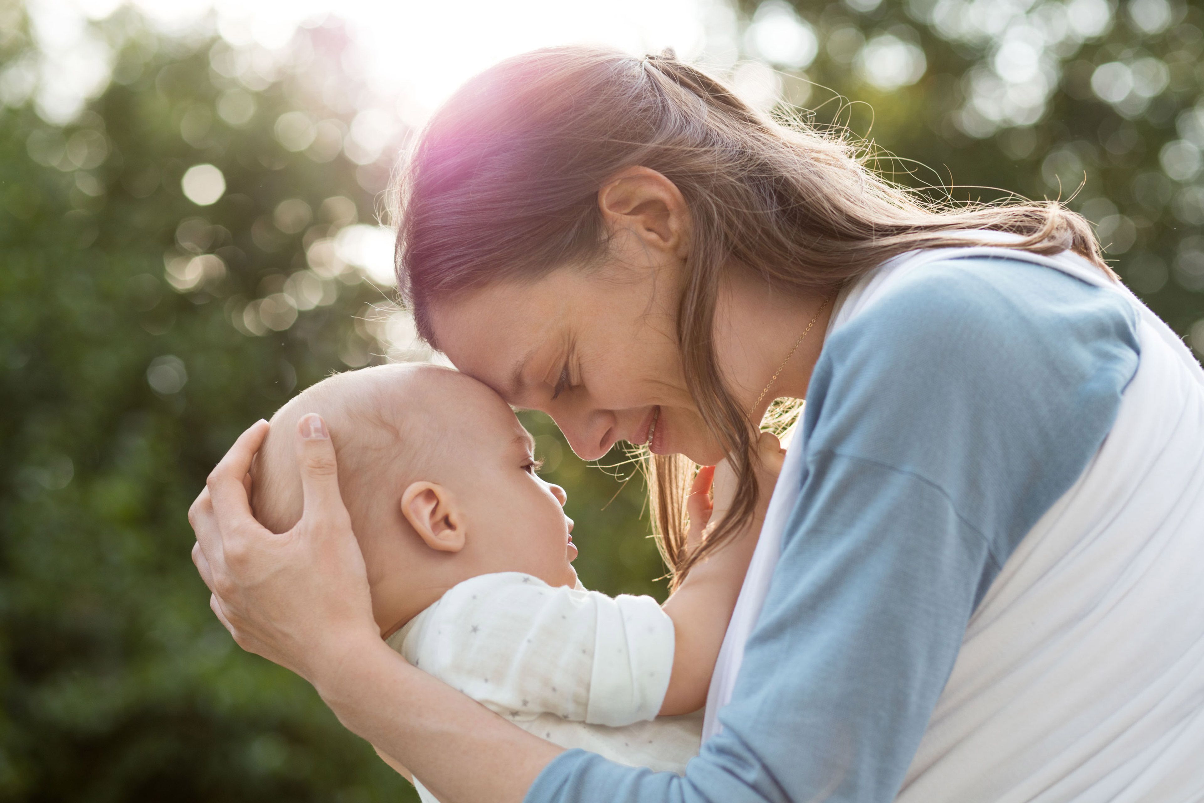 Ein zärtlicher Moment zwischen einer Mutter und ihrem Baby, in dem sie inmitten einer Naturkulisse einen intimen Blick miteinander teilen.