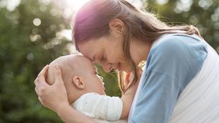 Ein zärtlicher Moment zwischen einer Mutter und ihrem Baby, in dem sie inmitten einer Naturkulisse einen intimen Blick miteinander teilen.