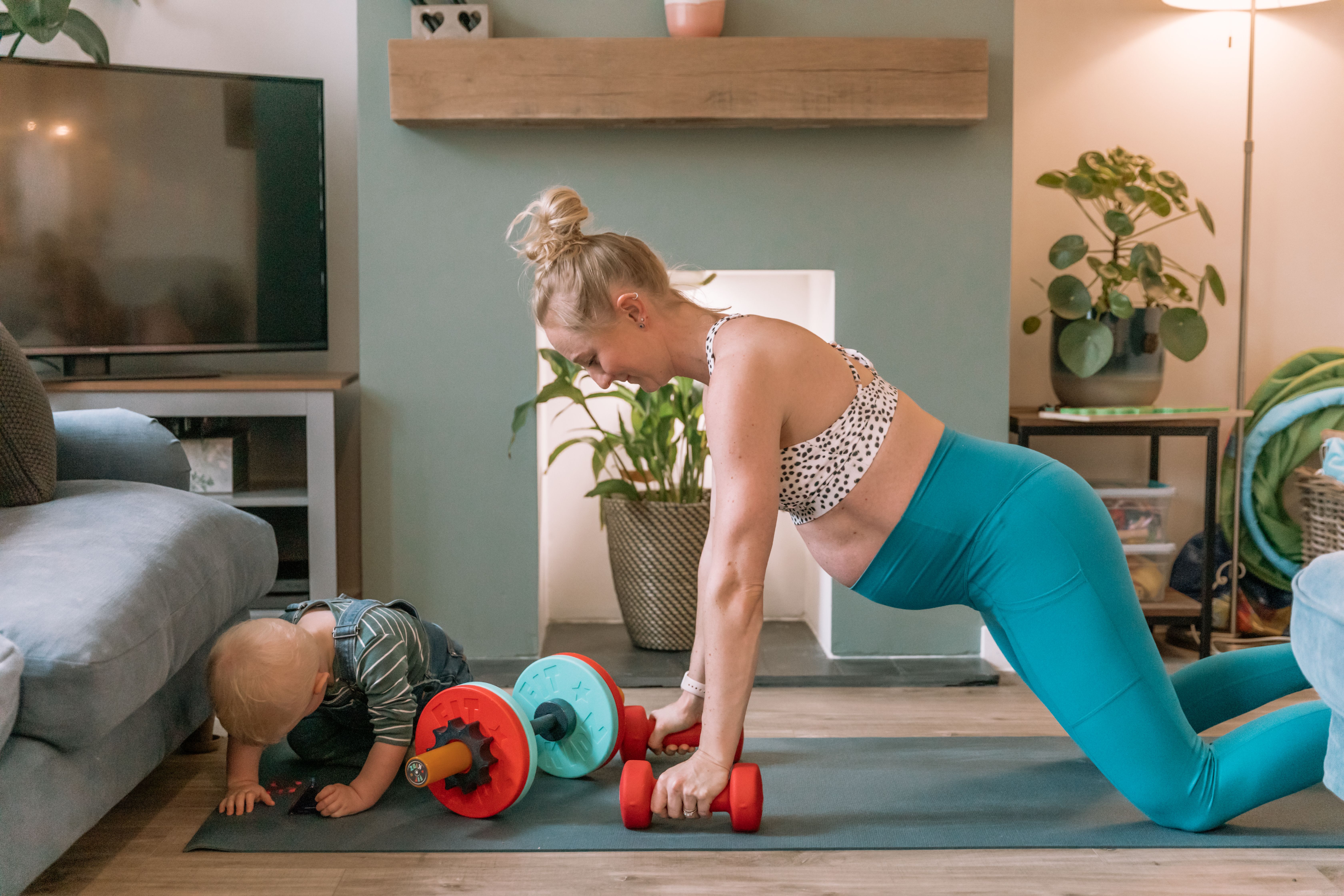 Pregnant mum doing a home workout beside her baby playing on the mat, showing a fun, active Bumps & Burpees moment