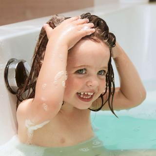 Ein kleines Kind in einer Badewanne, das mit Seifenblasen spielt und sein Haar hält.