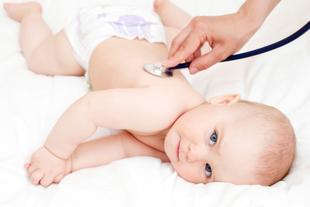 Ein Baby, das auf einer weißen Fläche liegt und ein Stethoskop auf dem Rücken trägt, wobei eine Hand das Stethoskop hält.