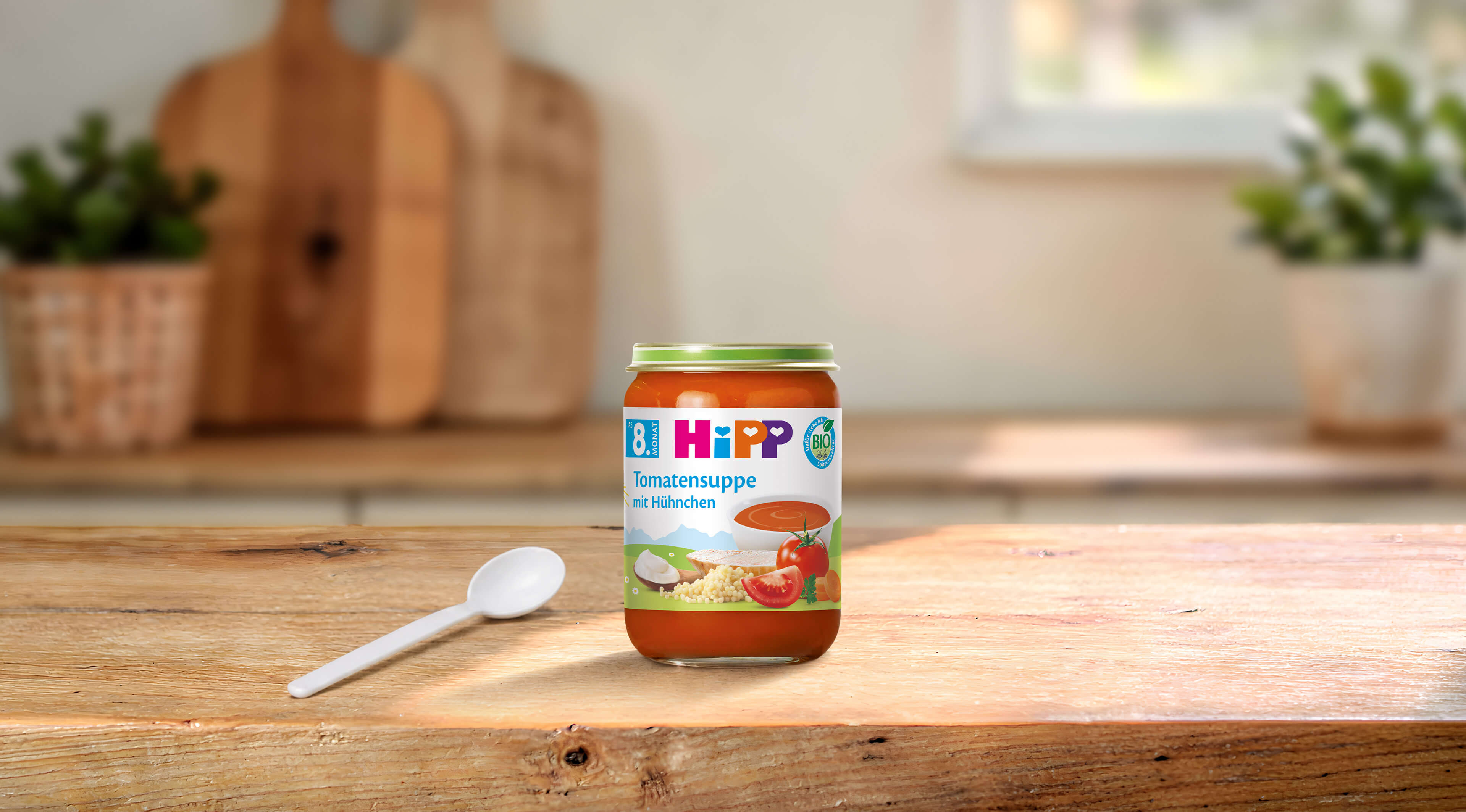 HiPP Bio Tomatensuppe mit Hühnchen im Glas für Babys ab 8. Monat auf Holztisch mit Löffel in heller Küche
