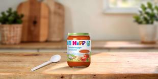 HiPP Bio Tomatensuppe mit Hühnchen im Glas für Babys ab 8. Monat auf Holztisch mit Löffel in heller Küche