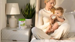 Mum feeding her baby HiPP Organic follow on milk on the bed