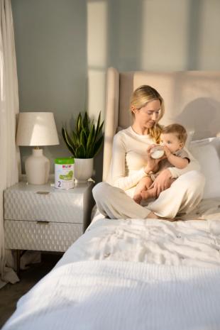 Mum feeding her baby HiPP Organic follow on milk on the bed
