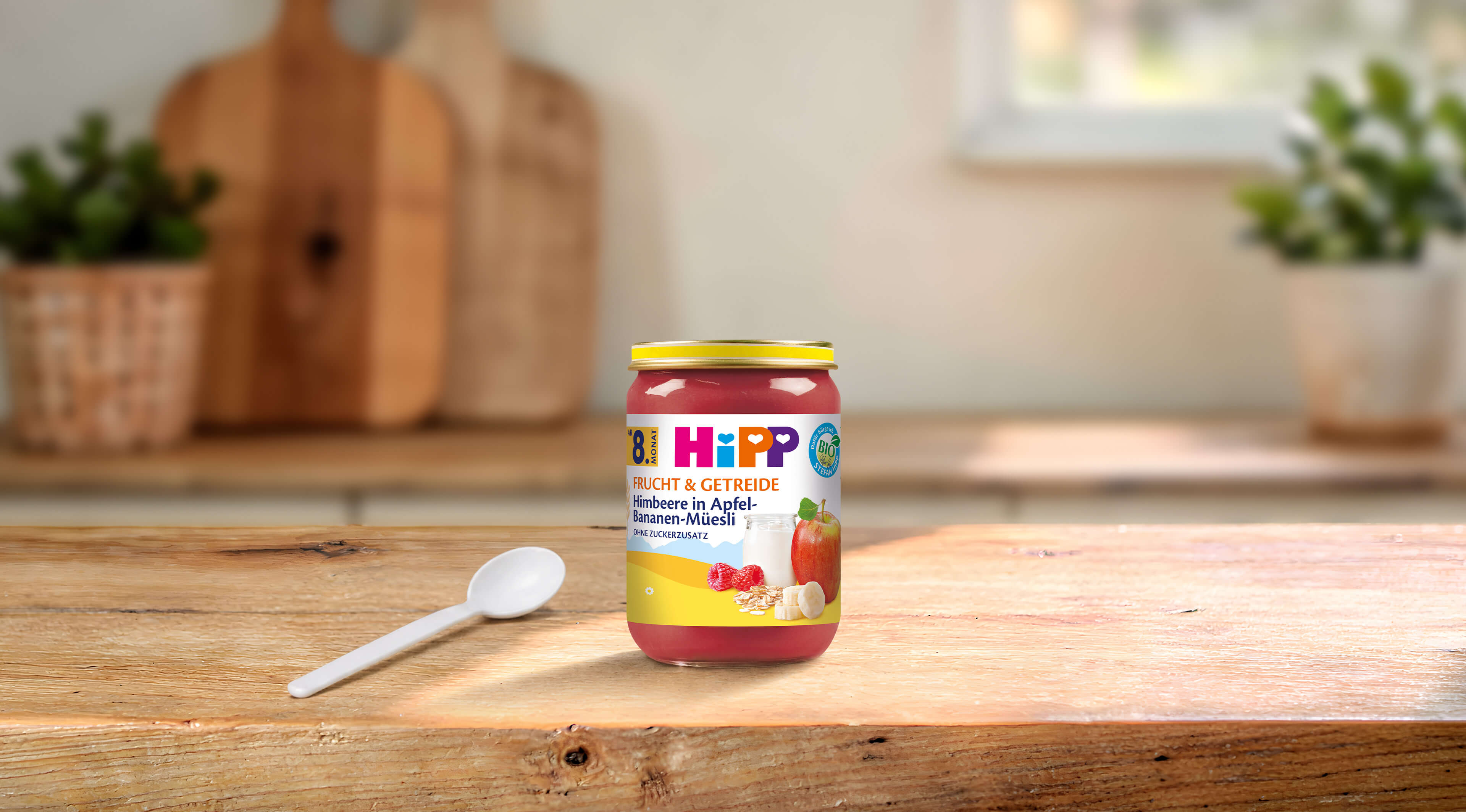 HiPP Bio-Glas Himbeere in Apfel-Bananen-Müesli ab 8 Monaten auf Holztisch mit Löffel in heller Küche