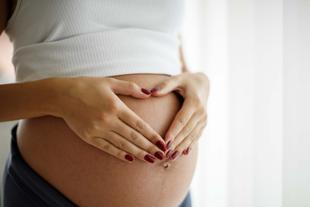 Die Hände einer Person bilden eine Herzform über dem schwangeren Bauch.