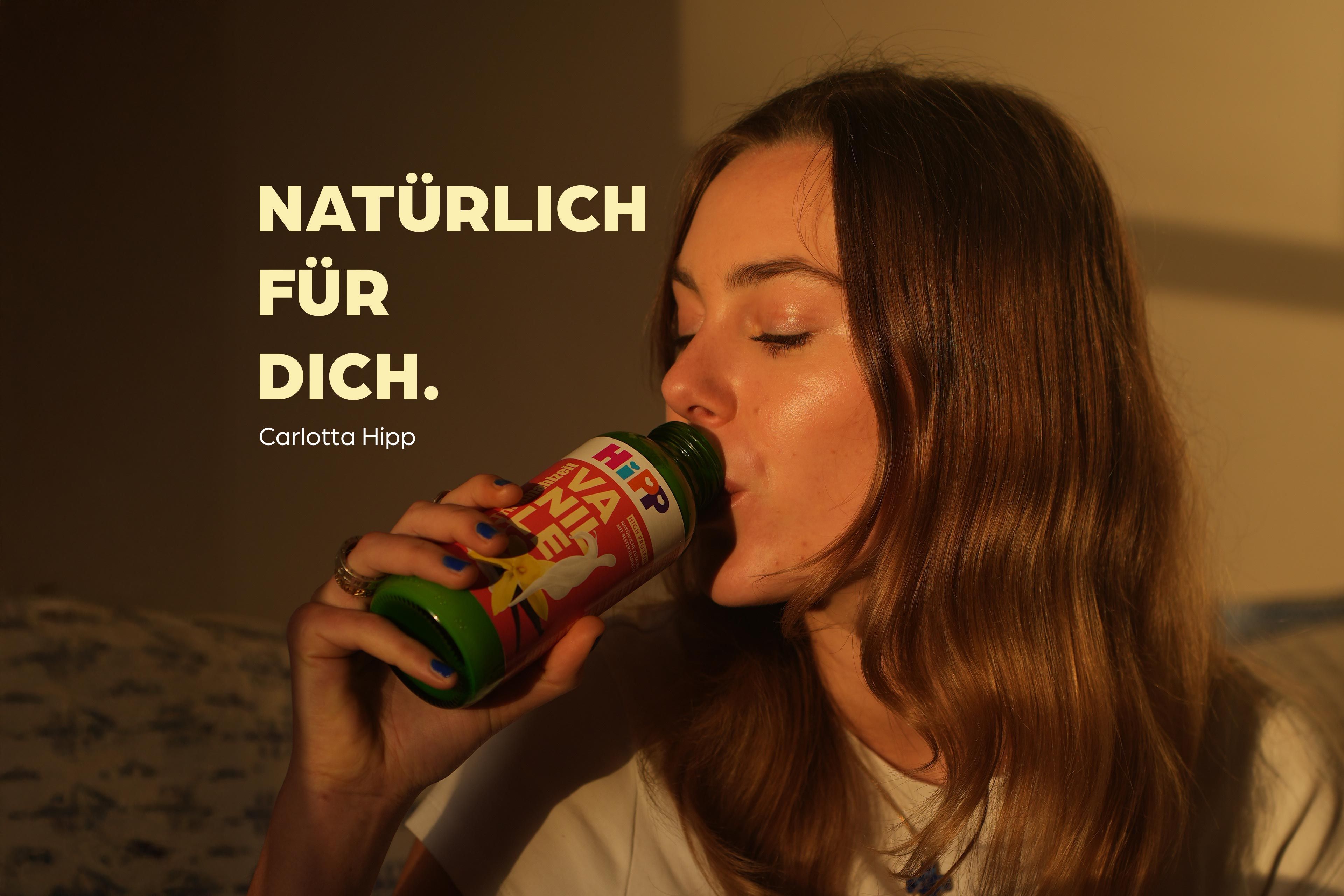 Junge Frau trinkt entspannt eine HiPP Trinkmahlzeit aus der Flasche, daneben der Schriftzug „Natürlich für dich.“