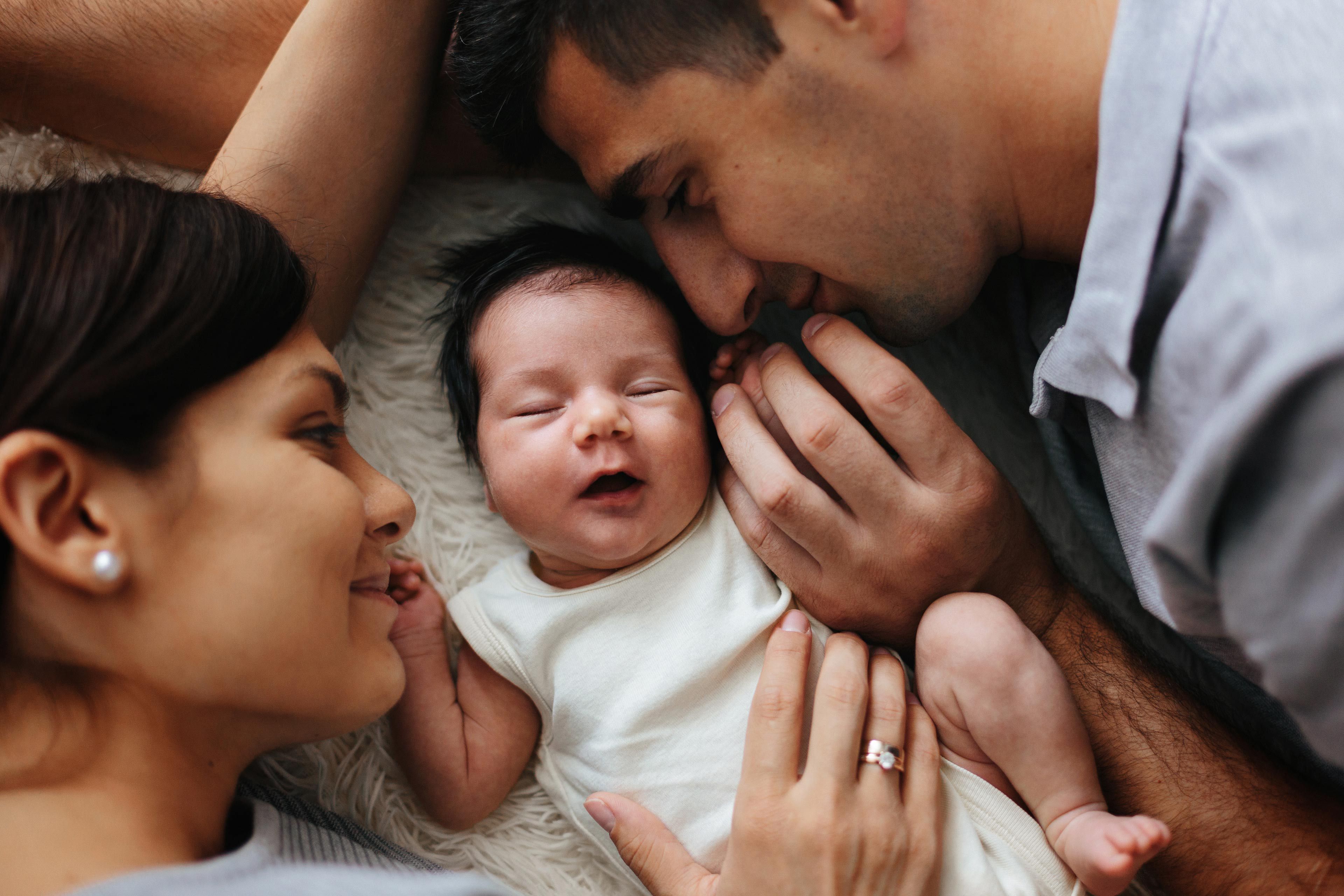 Ein zärtlicher Moment zwischen einer Mutter, einem Vater und ihrem neugeborenen Baby, das gemütlich zwischen ihnen ruht.