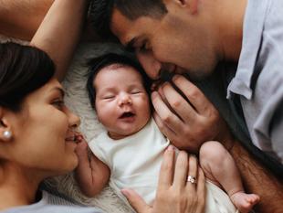 Ein zärtlicher Moment zwischen einer Mutter, einem Vater und ihrem neugeborenen Baby, das gemütlich zwischen ihnen ruht.