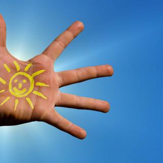 Geöffnete Hand mit gelber, lachender Sonne auf der Handfläche vor strahlend blauem Himmel als Symbol für Vitamin D
