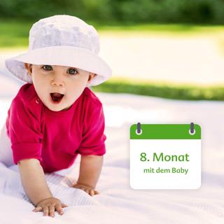 Ein Baby, bekleidet mit einem rosafarbenen Kleid und einem weißen Hut, liegt auf einer Decke im Freien und hat ein großes Kissen neben sich.
