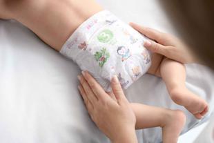 Der Rücken eines Babys, das eine Windel mit verschiedenen Cartoon-Figuren trägt, wobei eine Hand sanft den Rücken des Babys berührt.