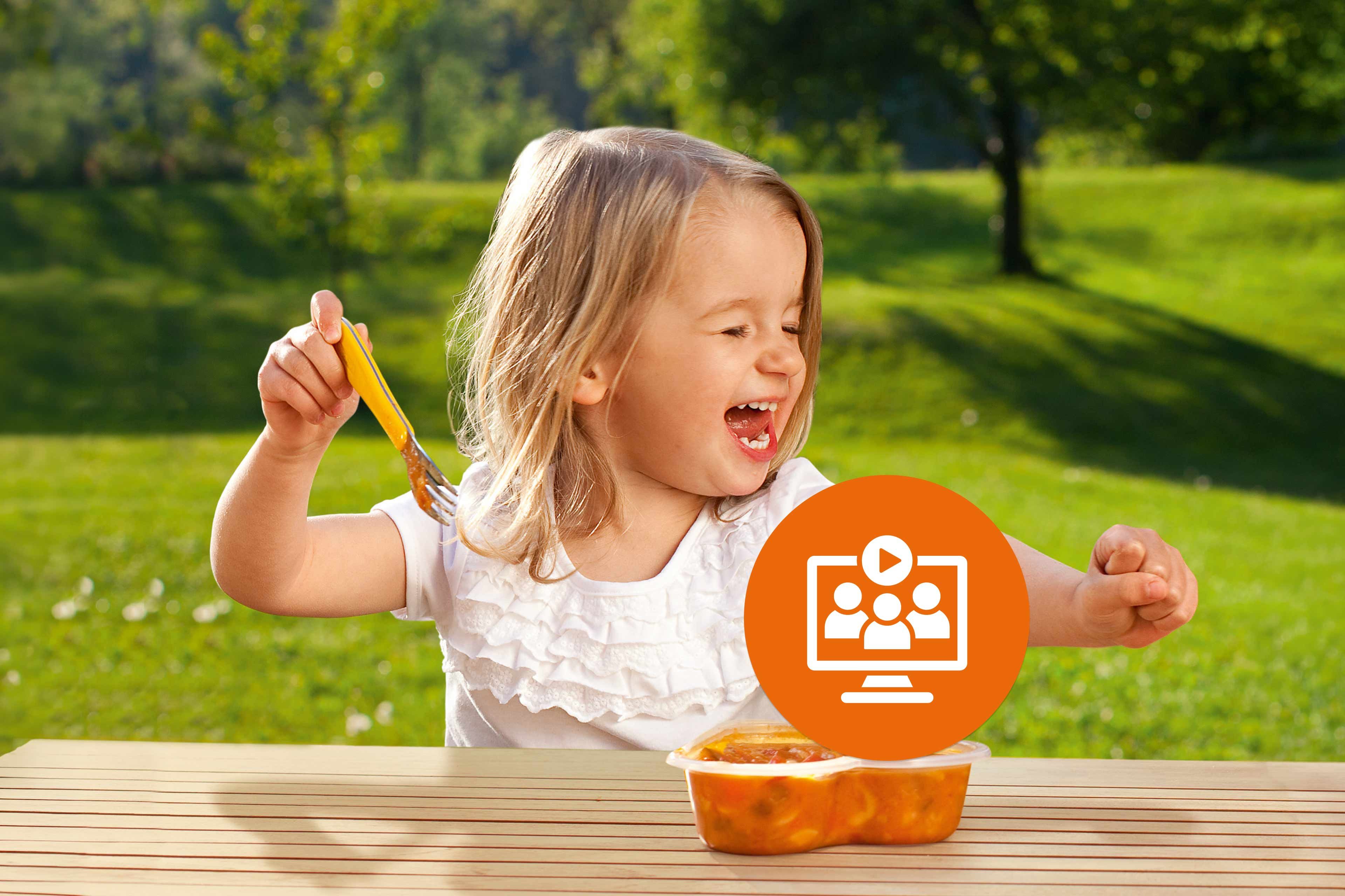 Lachendes Kleinkind isst draußen am Holztisch eine warme Mahlzeit, darüber ein orangefarbenes Webinar-Symbol eingeblendet.