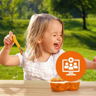 Lachendes Kleinkind isst draußen am Holztisch eine warme Mahlzeit, darüber ein orangefarbenes Webinar-Symbol eingeblendet.