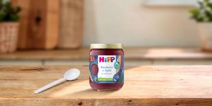 HiPP Bio-Gläschen „Blaubeere in Apfel“ ab 5. Monat auf Holztisch mit Löffel in heller, gemütlicher Küchenumgebung