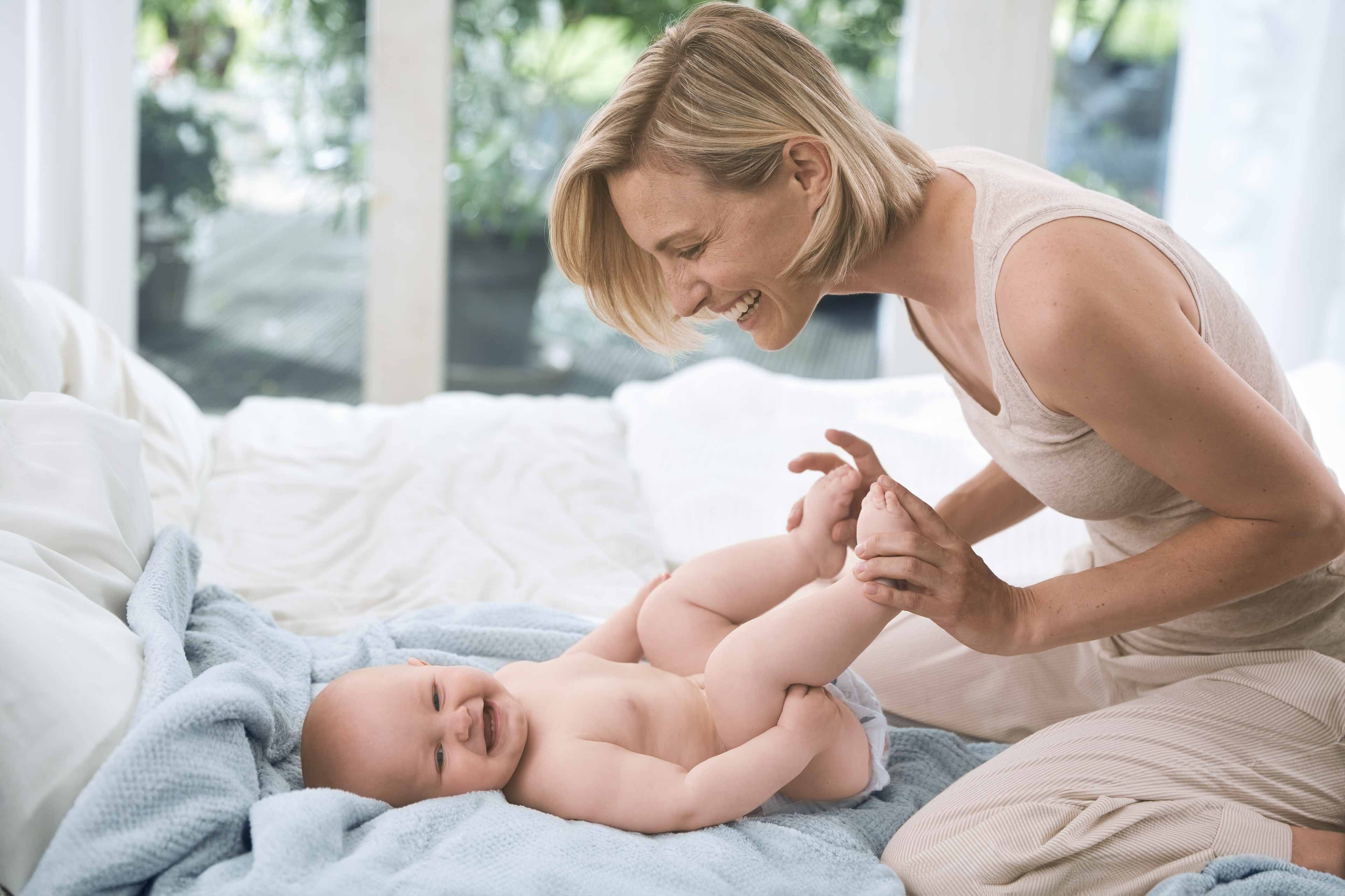Ein zärtlicher Moment zwischen einer Mutter und ihrem Baby, in dem die Mutter sanft die Füße des Babys hält und sie beide einen freudigen Moment miteinander teilen.