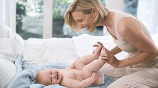 Ein zärtlicher Moment zwischen einer Mutter und ihrem Baby, in dem die Mutter sanft die Füße des Babys hält und sie beide einen freudigen Moment miteinander teilen.