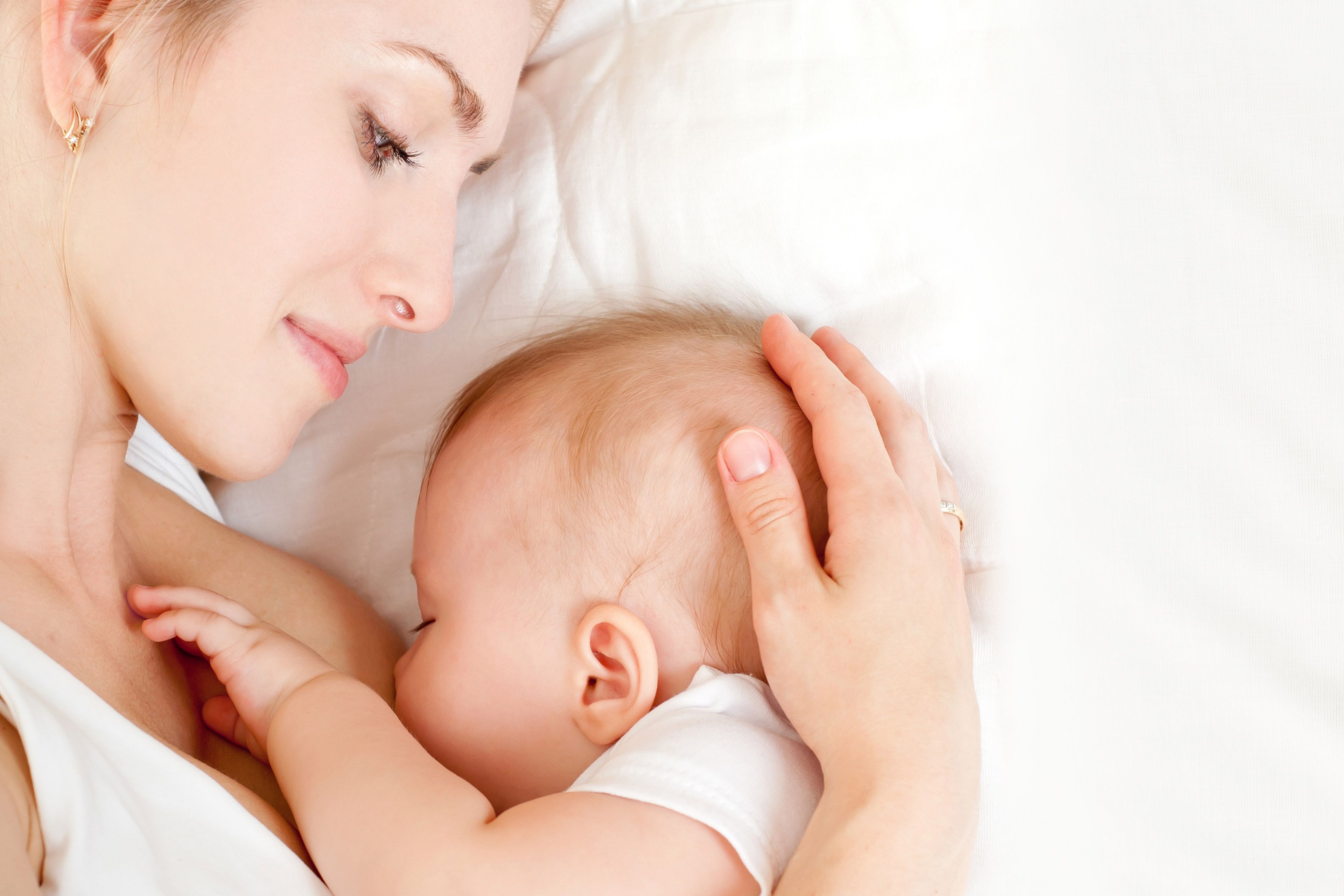 Ein zärtlicher Moment zwischen einer Mutter und ihrem Baby, in dem die Mutter sanft den Kopf des Babys berührt, während das Baby an ihrer Brust ruht.