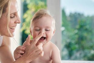 Ein zärtlicher Moment zwischen einer Mutter und ihrem Baby, in dem die Mutter spielerisch das Gesicht des Babys berührt, was eine freudige Reaktion hervorruft.