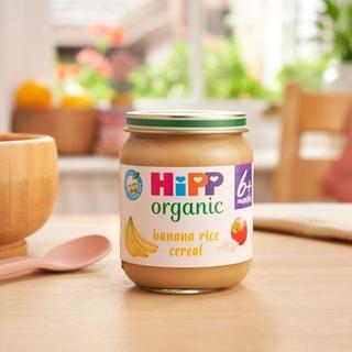 HiPP Organic Banana Rice Cereal jar on a dining table next to a bowl and spoon