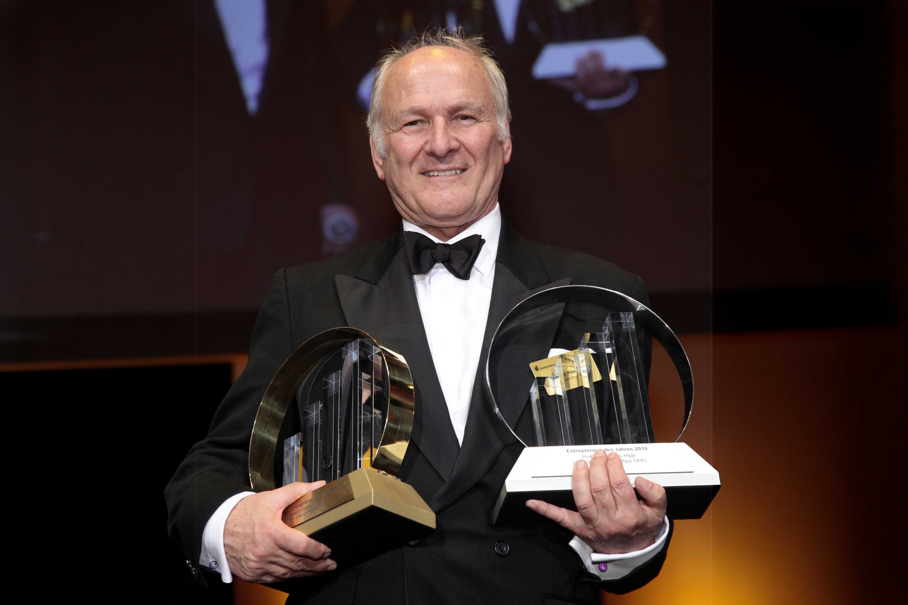 Claus Hipp im schwarzen Anzug mit zwei Awards in der Hand