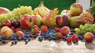Eine Vielzahl von frischen Früchten und Beeren, die auf einer hölzernen Oberfläche angeordnet sind, darunter Äpfel, Bananen, Trauben, Birnen, Erdbeeren, Heidelbeeren und eine Ananas.
