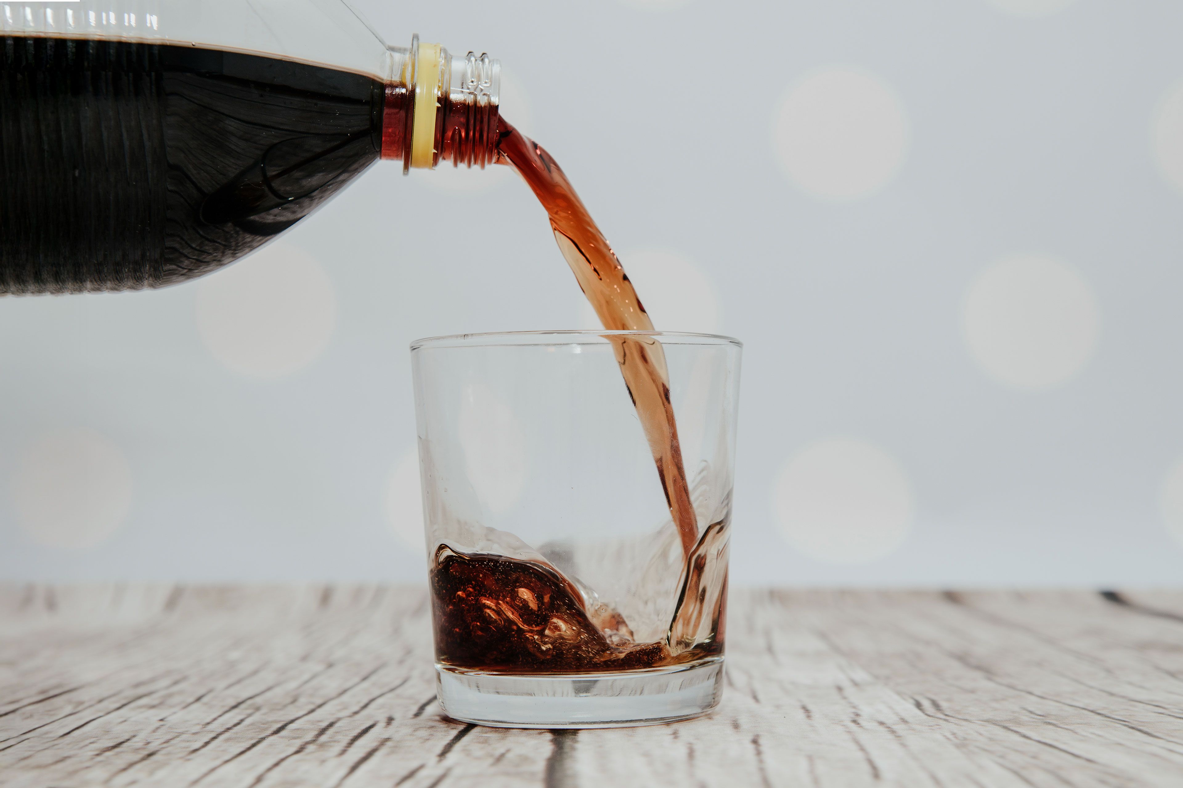 Ein klares Glas, das mit einer braunen Flüssigkeit gefüllt ist, bei der es sich vermutlich um Soda handelt, wird aus einer dunklen Flasche gegossen.