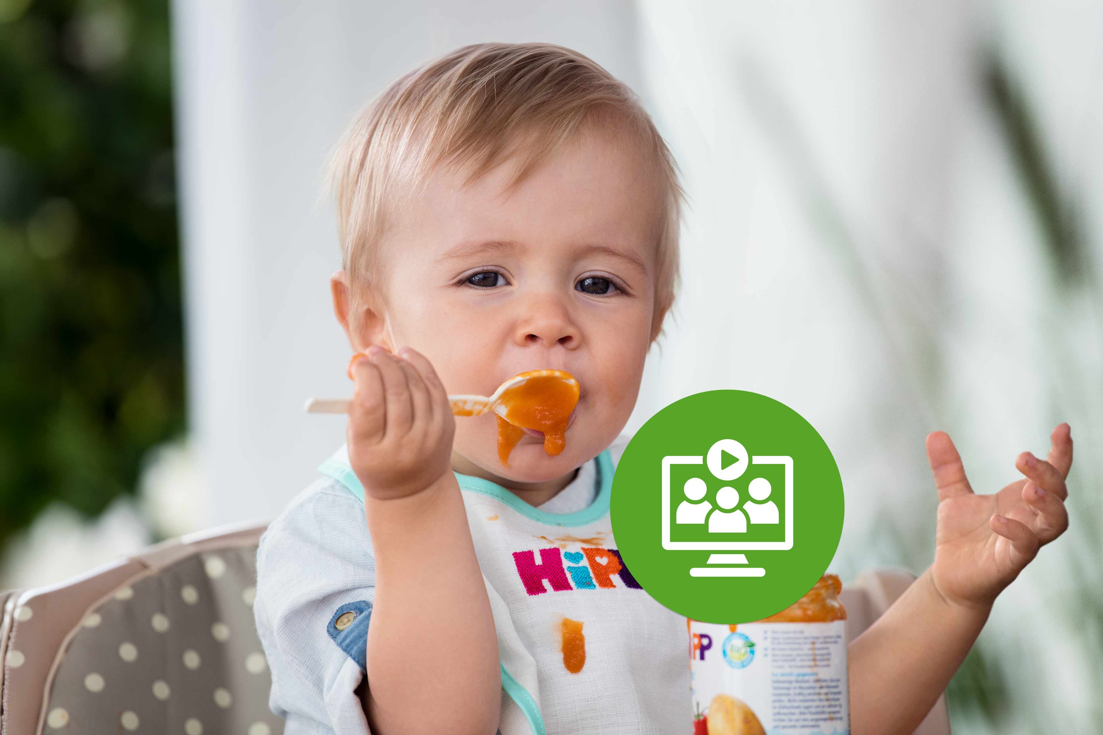 Baby sitzt im Hochstuhl, isst orangefarbenen Brei mit dem Löffel und trägt ein HiPP-Lätzchen, Symbol fürs Beikost-Webinar davor.