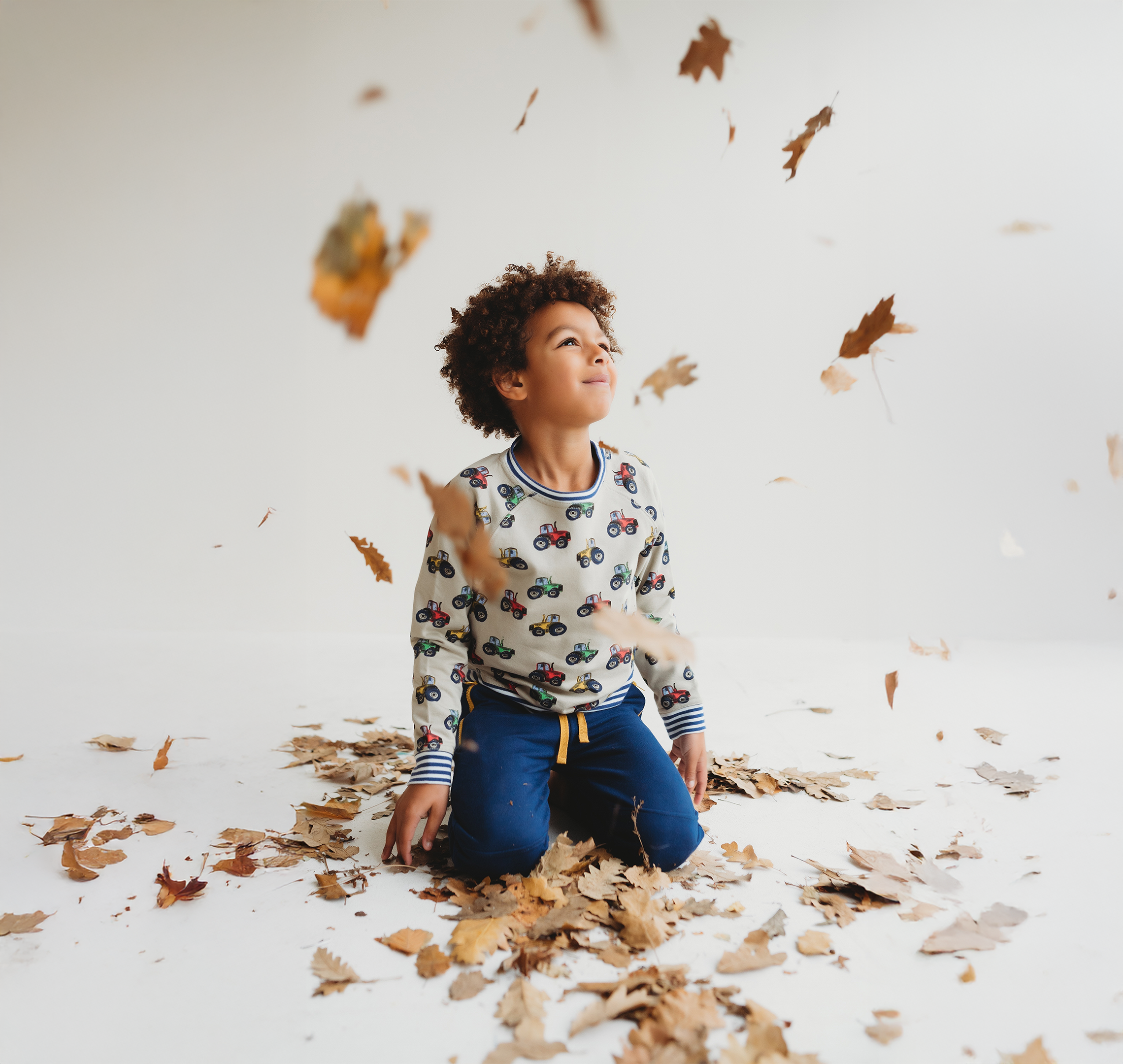 Young boy playing in leaves whilst wearing Lilly + Sid stone tractor top
