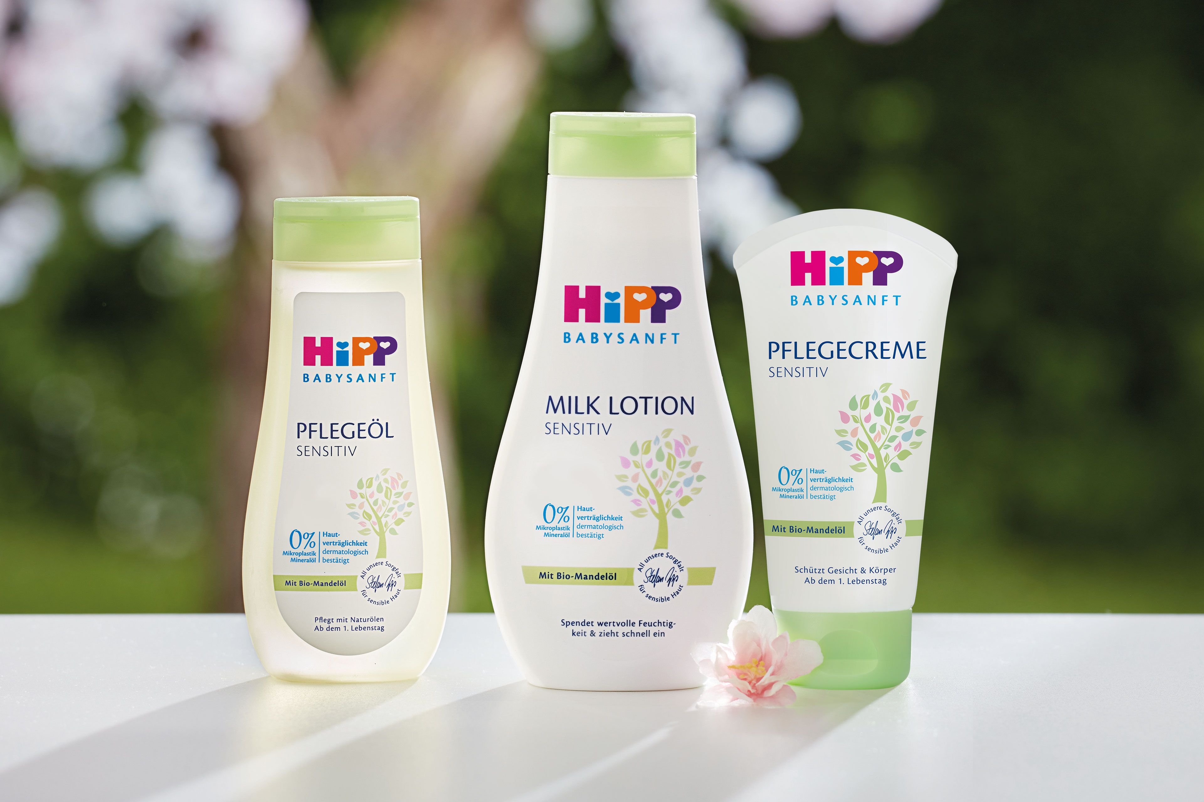 Eine Reihe von Babypflegeprodukten von Hipp, darunter eine Körperbutter, ein Massageöl und eine Körperlotion, die alle mit natürlichen Inhaltsstoffen gekennzeichnet sind und vor einer grünen Kulisse präsentiert werden.