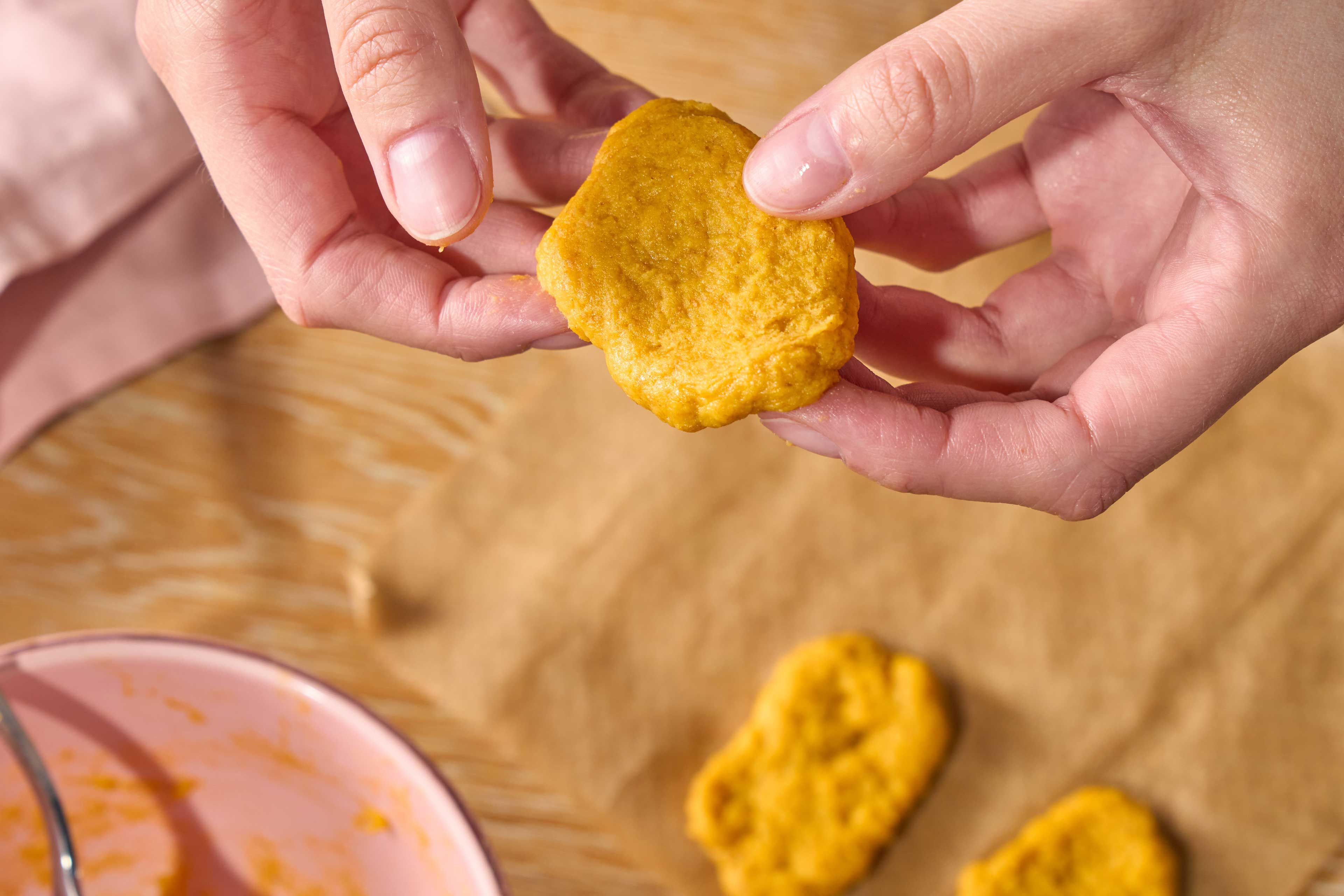 Hände halten ein rundes, gelbliches, unregelmäßig geformtes Gebäckstück