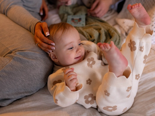 Smiling baby in floral pajamas lying on a bed, surrounded by family, conveying warmth and comfort.