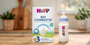 HiPP 3 BIO Combiotik® Folgemilch-Packung und gefülltes Babyfläschchen mit HiPP Logo auf Holztisch in heller Küche