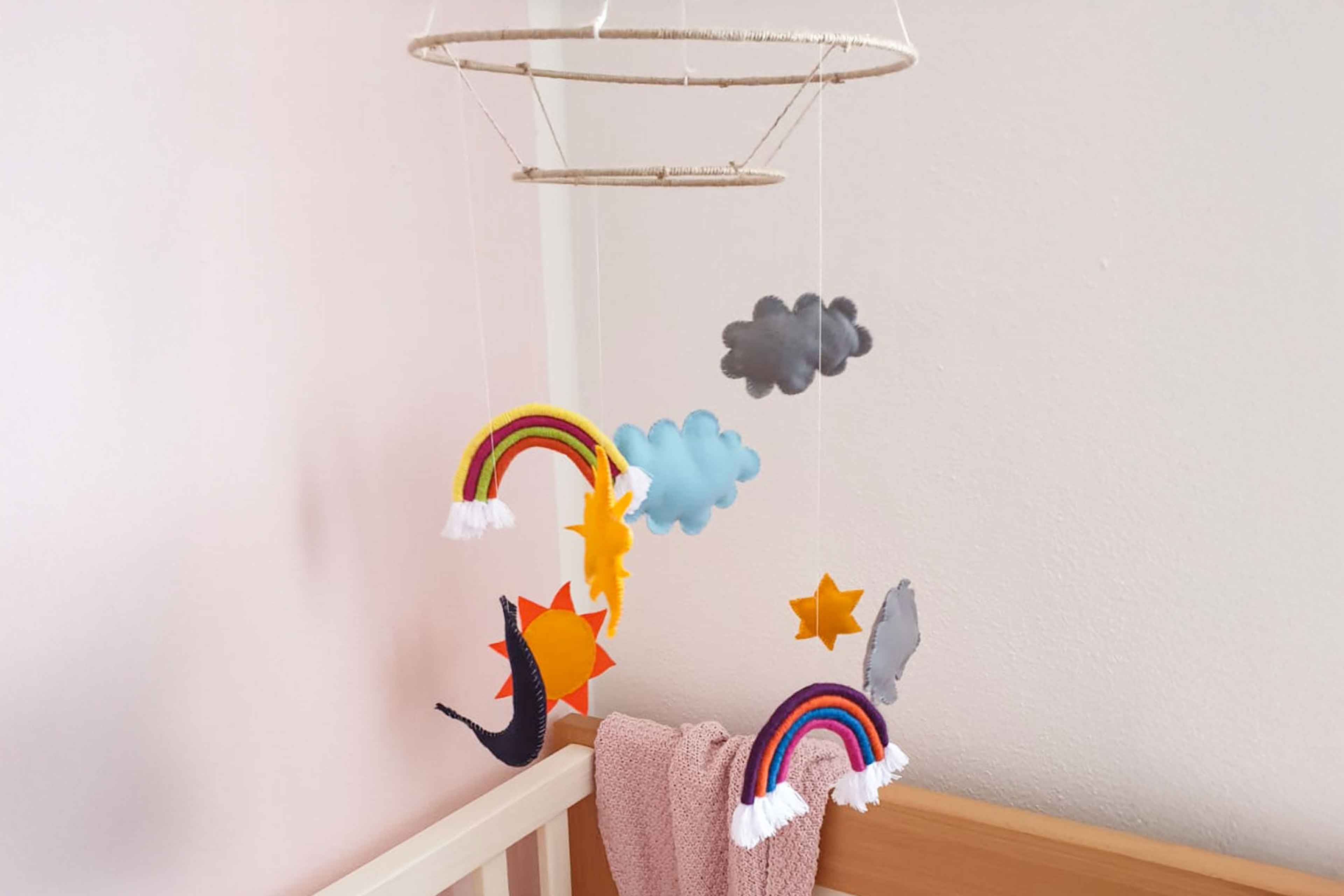 Ein Babyzimmer mit einem Mobile über dem Kinderbett, auf dem Regenbögen, Wolken und andere dekorative Elemente zu sehen sind.