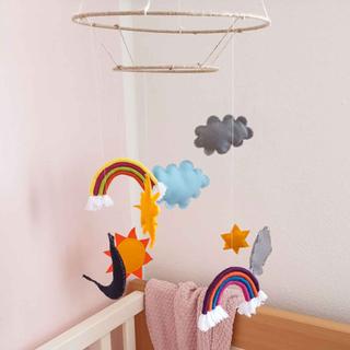 Ein Babyzimmer mit einem Mobile über dem Kinderbett, auf dem Regenbögen, Wolken und andere dekorative Elemente zu sehen sind.
