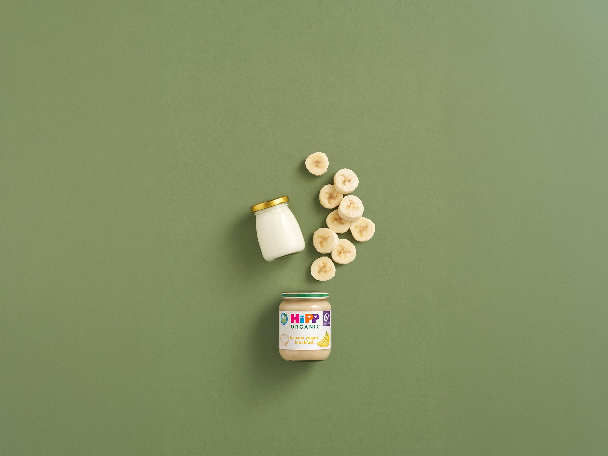 HiPP Organic Banana Yogurt Breakfast jar with sliced banana and plain yogurt jar on a green background