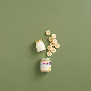 HiPP Organic Banana Yogurt Breakfast jar with sliced banana and plain yogurt jar on a green background