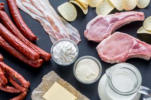 Eine Vielzahl von Fleischprodukten, darunter Würstchen, Speck und Schweinekoteletts, begleitet von Milchprodukten wie Sahne und Butter und einigen Snack-Chips.