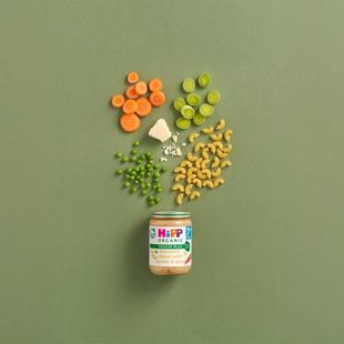 HiPP Organic Macaroni Cheese with Carrots & Peas jar surrounded by pasta, carrots, peas, leeks and cheese on a green background