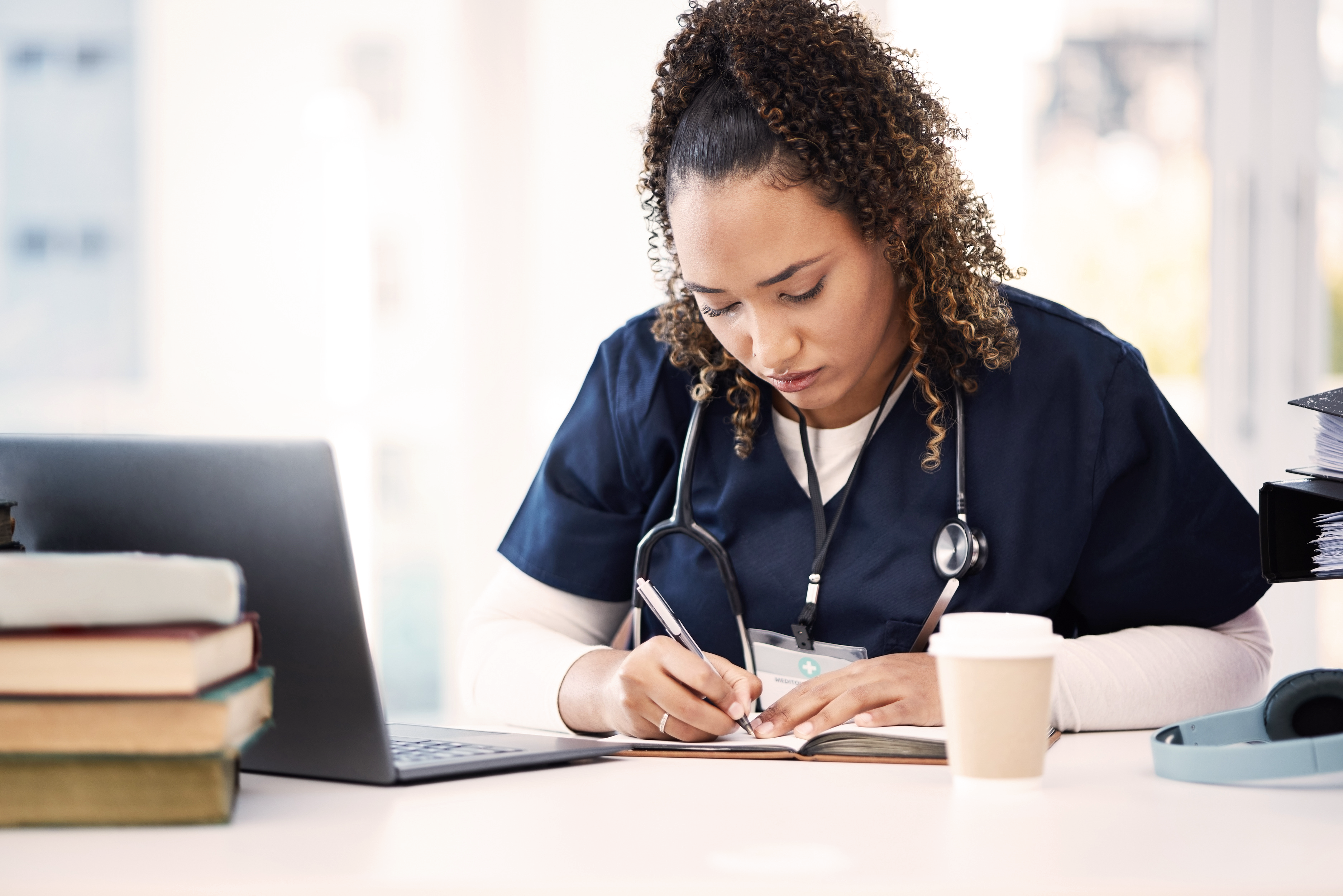 Healthcare professional studying at a desk, writing notes beside a laptop as part of continued professional development