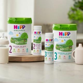 HiPP Organic follow on and growing up milks on a bright kitchen worktop beside a baby bottle and pastel sippy cup