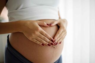 Schwangere Frau legt Hände mit roten Fingernägeln in Herzform auf ihren nackten Bauch