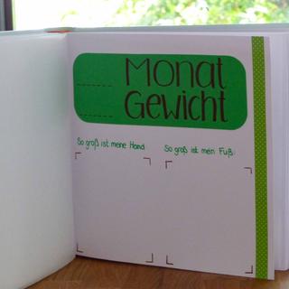 Ein grünes Heftchen mit dem Titel 'Monat Gewicht' mit zwei leeren Abschnitten zum Aufzeichnen des Gewichts, begleitet von einer Wäscheklammer auf der linken Seite.